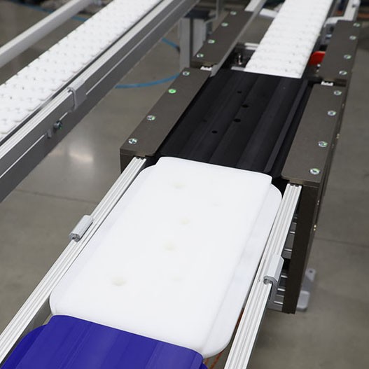 Three different color plastic pallets move between locating stations on a VersaFlex conveyor system.